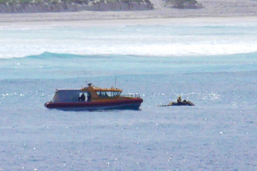 A search boat and a Jetsky resume the search for a missing person, sand dunes in the background. 