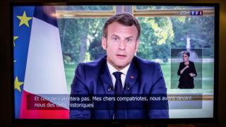 Emmanuel Macron delivering his address to the nation on a television screen