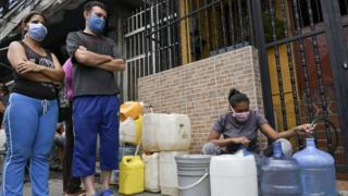 A woman fills a water container from a hose in Petare in Caracas