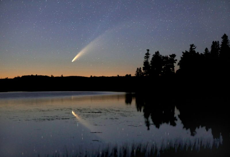 Comet in the sky above a lake, also reflecting in the lake.