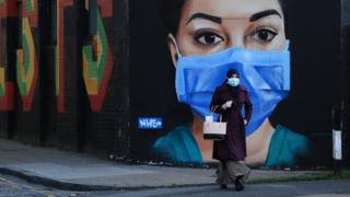 A woman wearing a mask walks in front of a mural of an NHS worker