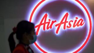 Woman wearing a face mask walks past the logo of AirAsia at Don Mueang Airport in Bangkok, Thailand.
