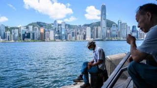 A man sits along the Kowloon side of Victoria Harbour which faces the skyline of Hong Kong Island.