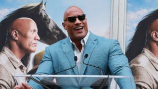 The Rock speaks at a podium during his latest film release