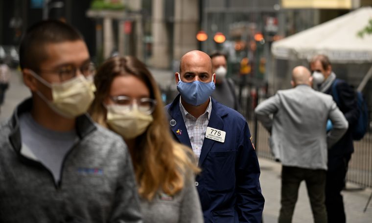 A trader walks in front of the New York Stock Exchange (NYSE) on May 26, 2020 at Wall Street in New York City. - Wall Street stocks surged early May 26, 2020 on optimism about coronavirus vaccines as the New York Stock Exchange resumed physical floor trading for the first time since late March. About five minutes into trading, the Dow Jones Industrial Average was up 2.3 percent at 25,023.76. The broad-based S&P 500 gained 2.0 percent to 3,013.04, while the tech-rich Nasdaq Composite Index advanced 1.6 percent to 9,468.96.The gains came after a ceremony presided over by New York Governor Andrew Cuomo, who wore a mask as he rung the opening bell to signal the start of the day for traders, also clad in masks and separated by plexiglas. (Photo by Johannes EISELE / AFP) (Photo by JOHANNES EISELE/AFP via Getty Images)