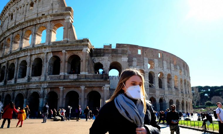 Tourist wearing a protective respiratory mask tours outside the Colosseo monument (Colisee, Coliseum) in downtown Rome on February 28, 2020 amid fear of Covid-19 epidemic. - Since February 23, more than 50,000 people have been confined to 10 towns in Lombardy and one in Veneto -- a drastic measure taken to halt the spread of the new coronavirus, which has infected some 400 people in Italy, mostly in the north. (Photo by Andreas SOLARO / AFP) (Photo by ANDREAS SOLARO/AFP via Getty Images)