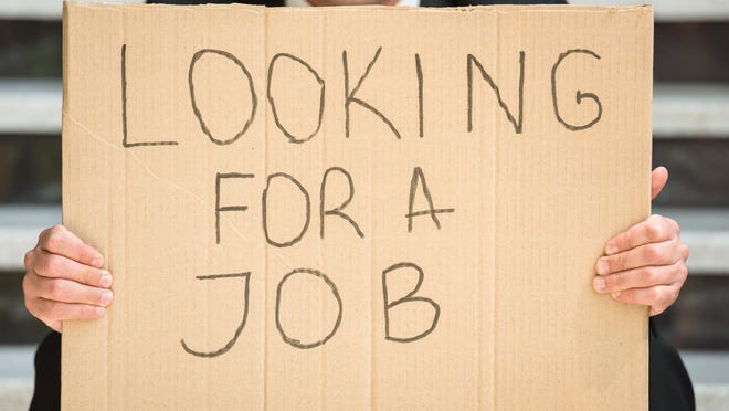 A businessman in a suit holding up a cardboard sign that reads, Looking for a job.