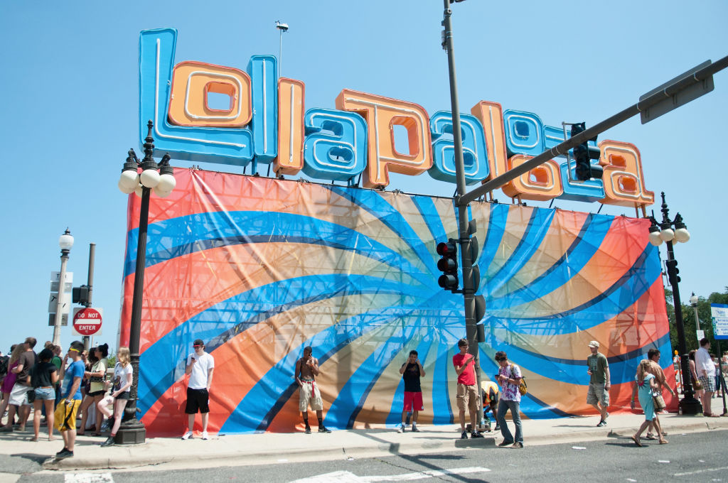 Wall with logos of Lollapalooza and some of the surrounding people at the entrance to the festival.