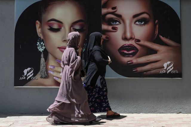 Burqa-clad women walk in front of portraits of other made-up women in Kabul, August 7, 2021