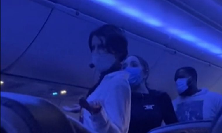 Woman is stopped in flight while using microphone to explain "true origin" of Covid