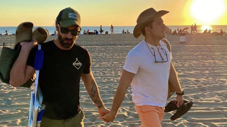 Marco Calvani and Marco Pigosi holding hands on the beach