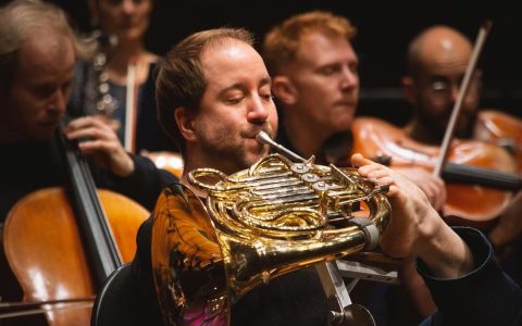 A musician playing the horn with his feet in a prestigious orchestra.  look how good