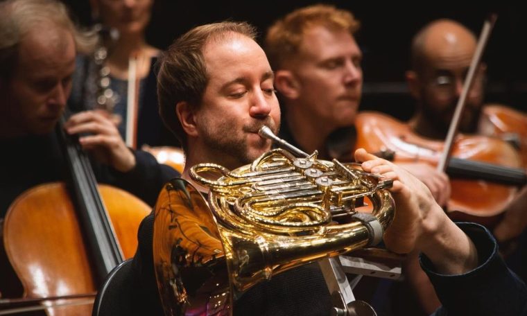 A musician playing the horn with his feet in a prestigious orchestra.  look how good